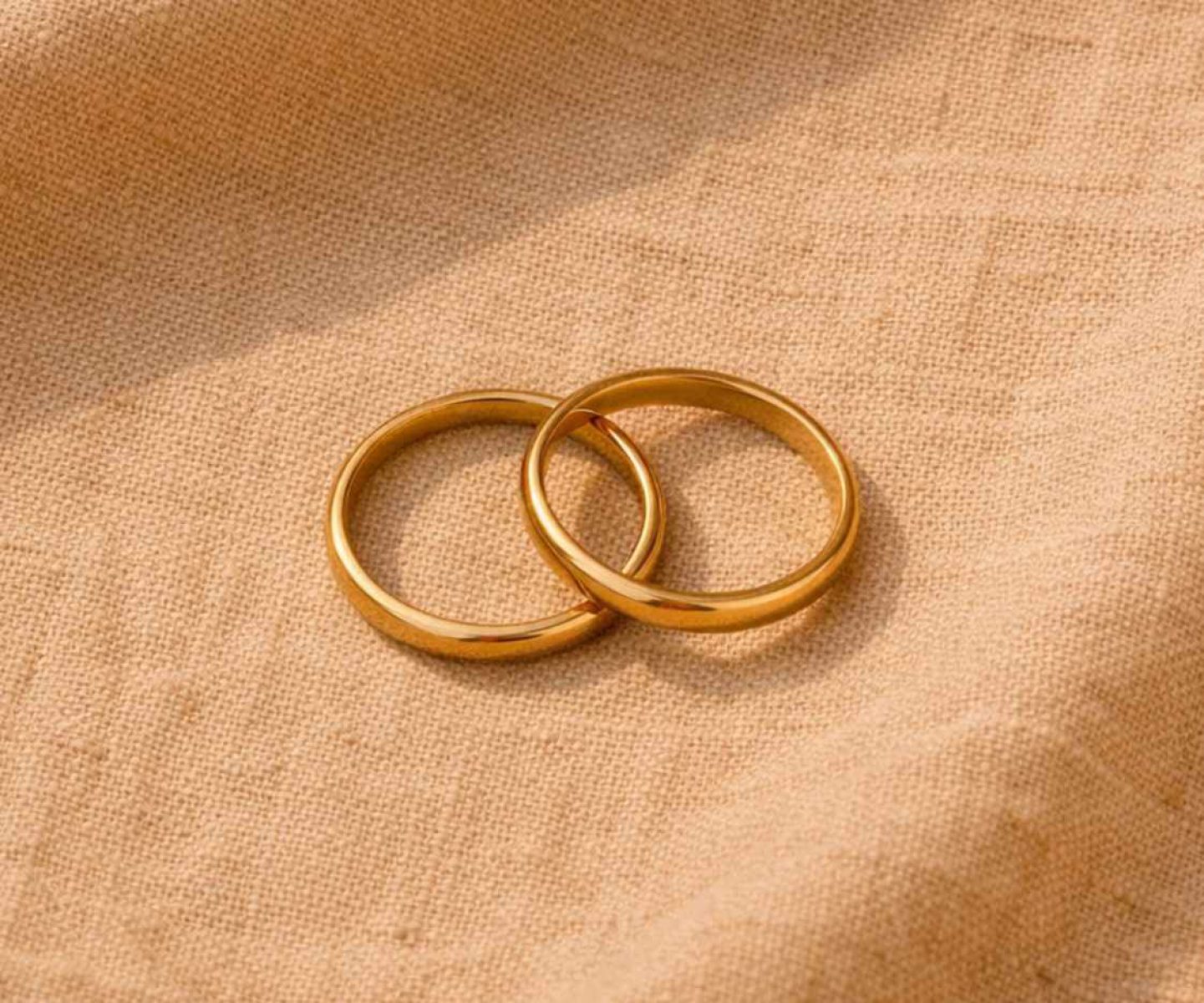 Zwei goldene Eheringe auf warmem Leinenstoff